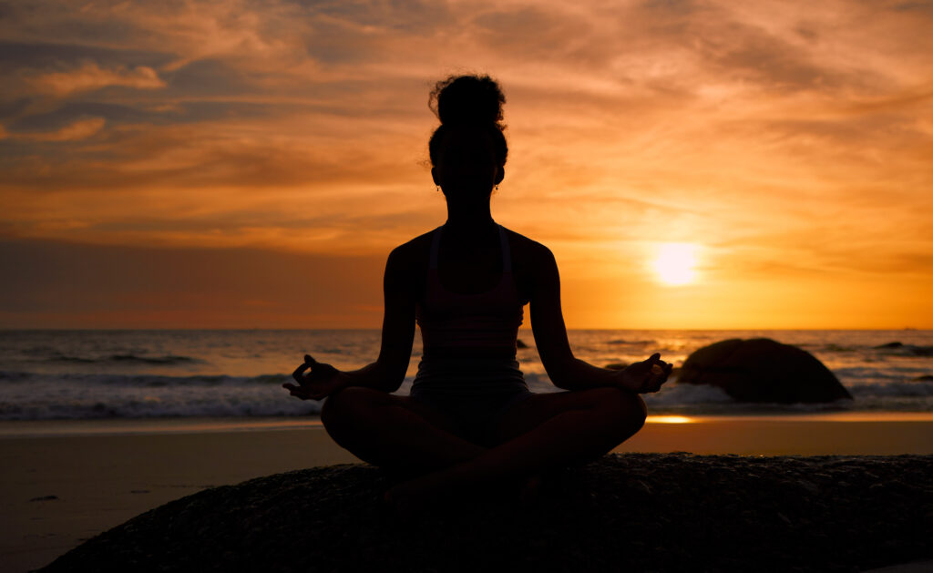 Image of person meditating at the beach with sunsetting.